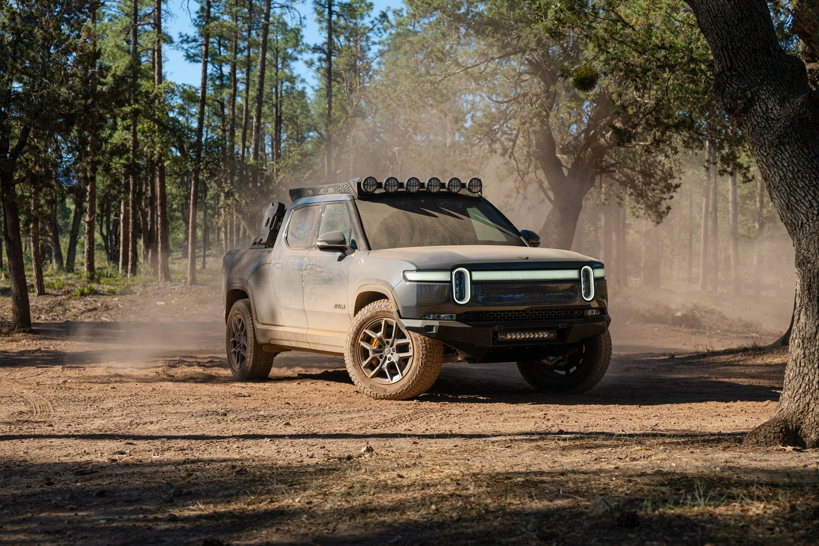 Rivian R1T in a dusty forest clearing with off road aftermarket parts.