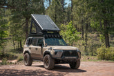 Roof top tent pitched up on a GX 550 fully equipped on camping trip. Visible are off road bumpers, a roof rack, tent, light brackets, and molle panels.