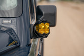 A close-up shot of Ditch Light Brackets for the 2022-2026 INEOS Grenadier & Quartermaster with auxiliary light mounted on the side mirror, with a blurred sandy road in the background.